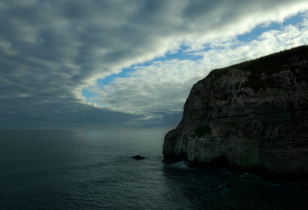 Robust cliff in the Atlantic ocean surrounded by an aura of blue sky amid dark clouds