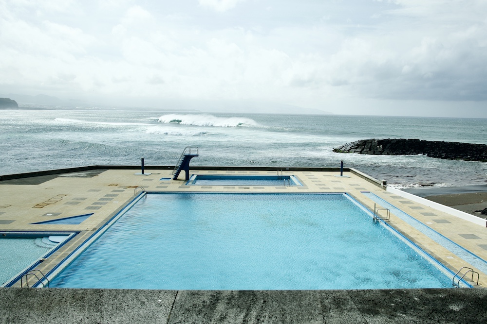 Swimmingpool with no people swimming in it and with the raw Atlantic Ocean in the background